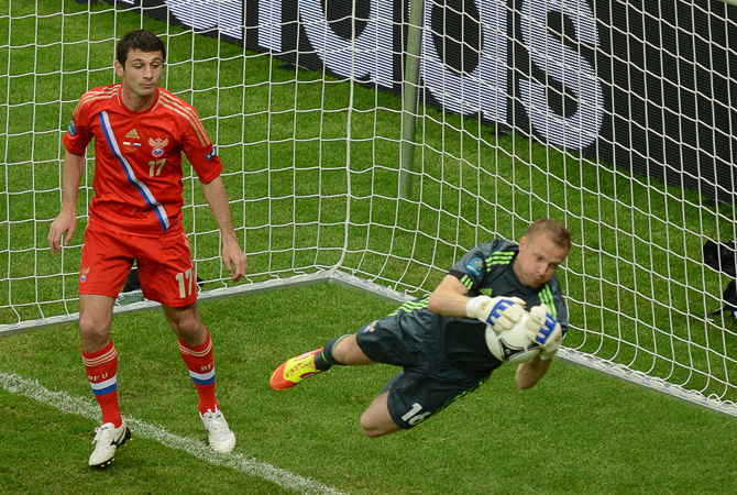 Russian goalkeeper Vyacheslav Malafeev grabs the ball next to Russian midfielder Alan Dzagoev.
