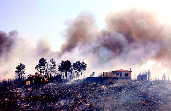 A view of a burnt house with smoke billowing in the background after the passage of a wildfire in Yatova, near Valencia on June 30, 2012. A forest fire in eastern Spain forced 700 people to evacuate their homes and indirectly caused a brief power cut at a nuclear plant, authorities said. The fire had burned 10 square kilometres of land in the Valencia region. ? Photo by AFP