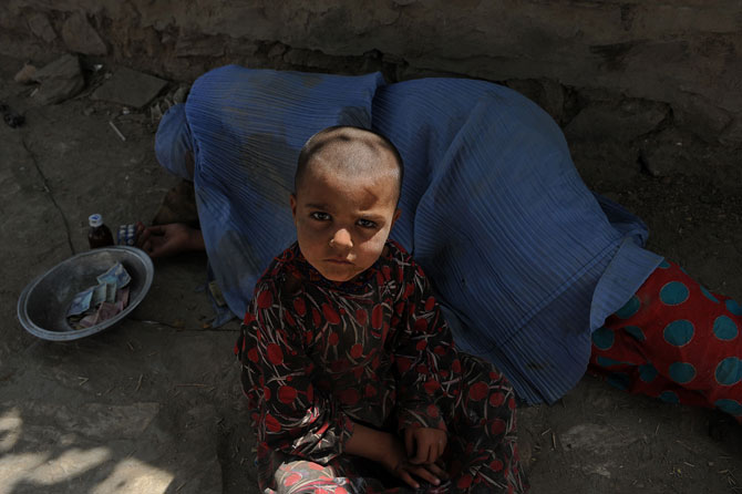 An Afghan woman begs while her child looks on at the roadside in Kabul on July 31, 2012 during the Islamic month of Ramadan. Throughout the month devout Muslims must abstain from food, drink and sex from dawn until sunset when they break the fast with the Iftar meal. ? Photo by AFP
