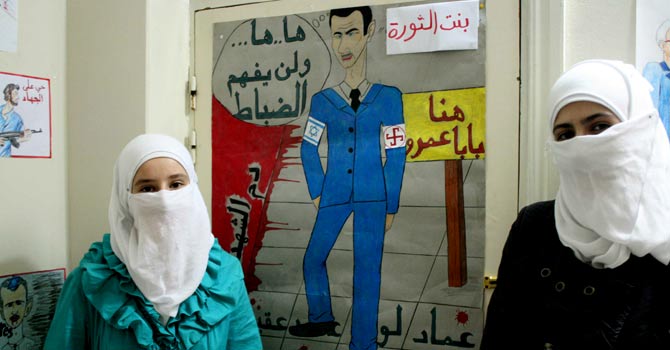 syria-artists-placards-afp-670 Two Syrian girls stand in front of a poster they drew, depicting Syrian leader Bashar al-Assad wearing two arm bands -- one with the Israeli flag and the other a Swastica (R) – in Qusayr on July 20, 2012. Some artists are dedicating themselves to the painting of images and writing of banner which are used during the weekly Friday protests against the regime of Syrian President Bashar al-Assad. – Photo by AFP
