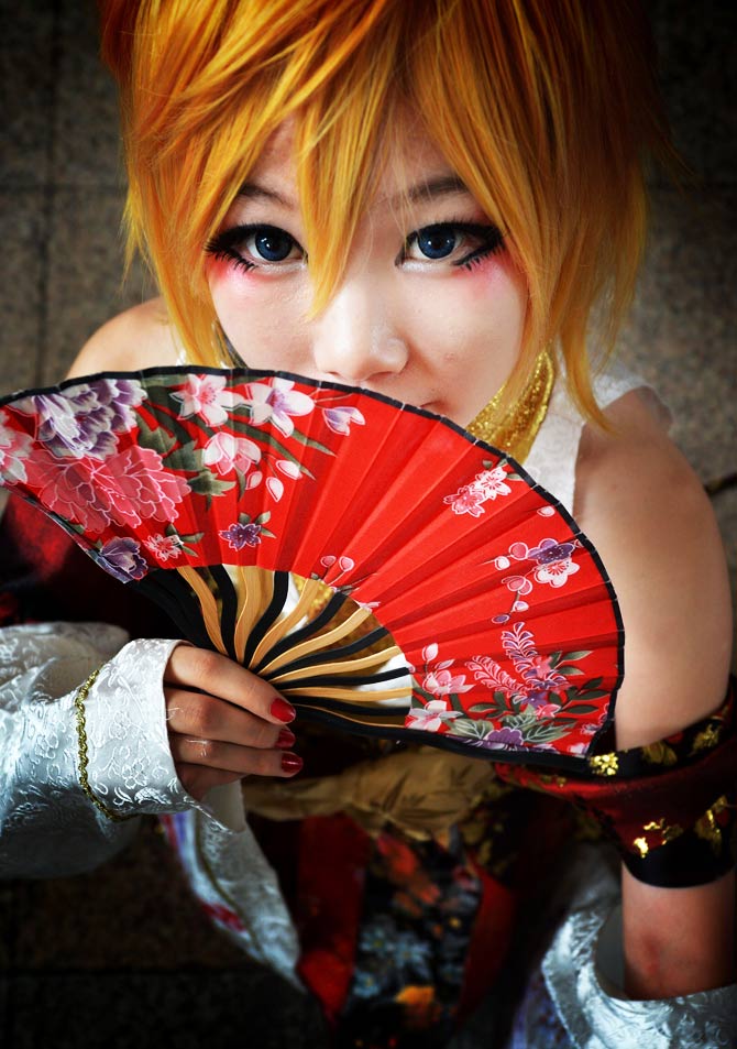 A cosplayer peeks from her crimson fan. - Photo by AFP