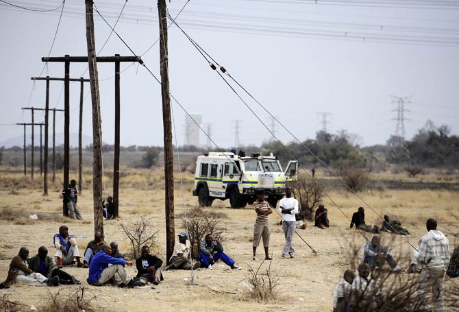 Miners gather in protest as a police vehicle surveys them from afar. – Photo by AFP