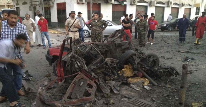 Members of the military and bystanders look at debris after a car bomb exploded near the offices of the military police in Tripoli