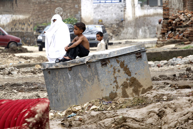 A boy sits on a trunk outside his collapsed house.
