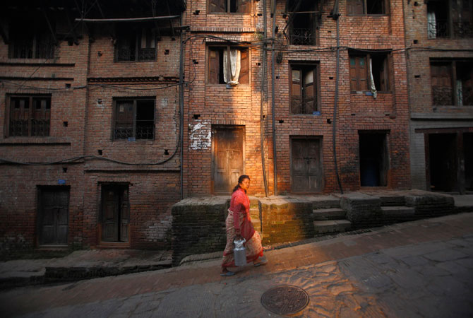A woman carrying a milk jar walks along a street in the ancient Nepalese city of Bhaktapur.