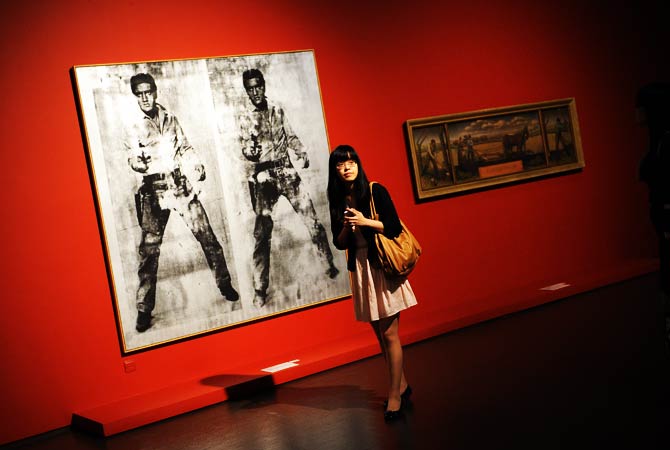 A woman walks past artwork of Elvis Presley (L) by US artist Andy Warhol. ? Photo by AFP