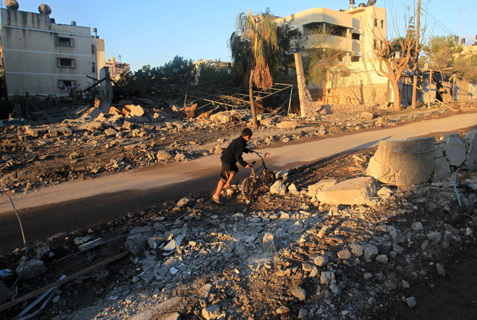 A Palestinian boy pushes his bycicle through the rubble in an area targeted by an Israeli.