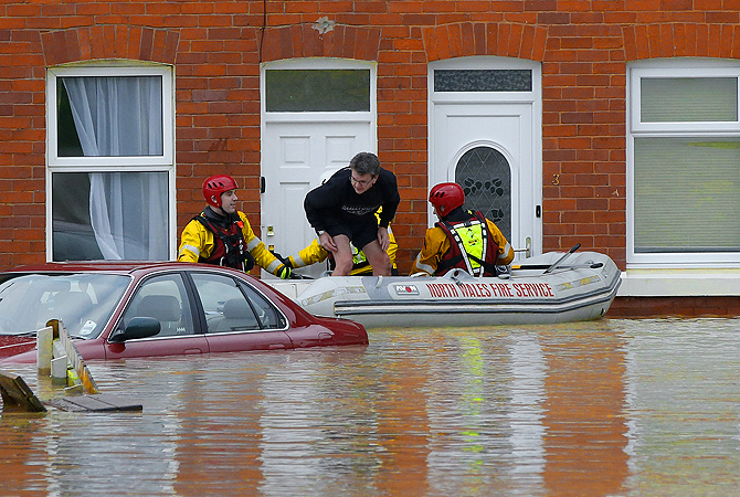 Firefighters in a boat rescue a stranded man from a house on a flooded street in St Asaph, north Wales.?Photo by Reuters
