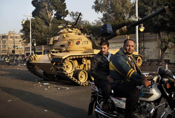 Two Egyptian men ride a motorbike past a tank stationed outside the presidential palace in Cairo.
