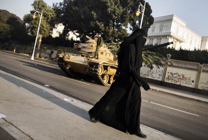 An fully-veiled Egyptian woman walks past an army tank parked outside the presidential palace in Cairo.