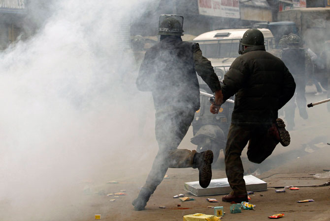 Indian policemen run for cover amid tear gas during clashes with supporters (unseen) of the Jammu Kashmir Liberation Front (JKLF) in Srinagar December 7, 2012.