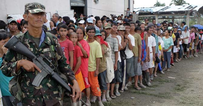 A soldier stands guard as typhoon evacuees queue for relief goods outside a local government town centre in New Bataan, Compostela Valley in southern Philippines – Photo by Reuters