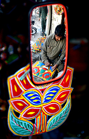 A Pakistani artisan reflected in a truck mirror works on making decorations for trucks and cars, in Rawalpindi. — AFP Photo