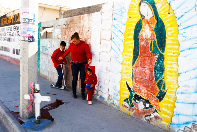 A woman walks with two children past a puddle of blood at a crime scene in Ciudad Juarez. ?Photo by Reuters