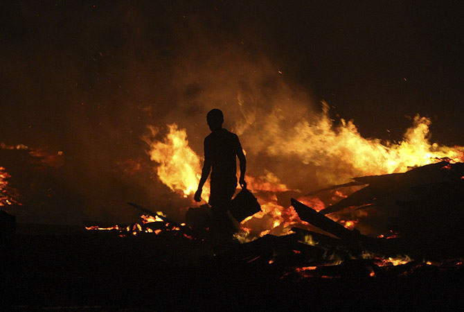 A man holds a bucket as he tries to extinguish a late night fire at the Okobaba sawmill near the Lagos Lagoon. Fire ripped through a poor suburb in Nigeria's biggest city Lagos on Tuesday, burning down ramshackle homes and workshops as firefighters fought to stop the blaze, a Reuters witness said. Dozens of buildings were burned to the ground in Ebute Metta, a community along the Lagos lagoon where sawmills process timber brought from across Nigeria.?Photo by Reuters