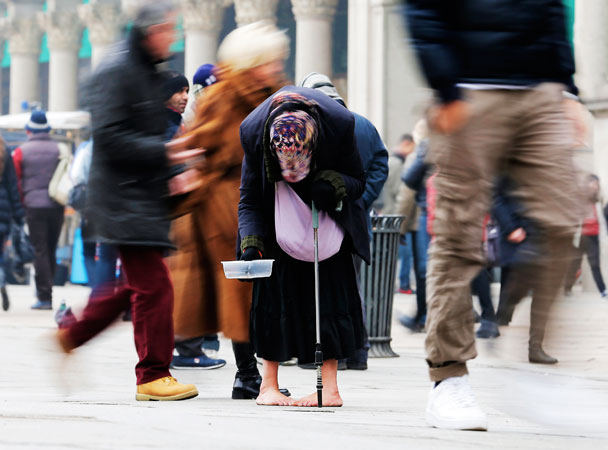 A woman begs for money amid passers-by in downtown Milan, Italy. -Photo by AP