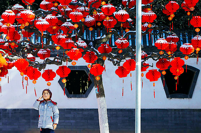 A boy poses for a photo under a tree decorated with red lanterns after a snowfall, at Ditan Park (the Temple of Earth) in Beijing. ?Photo by Reuters