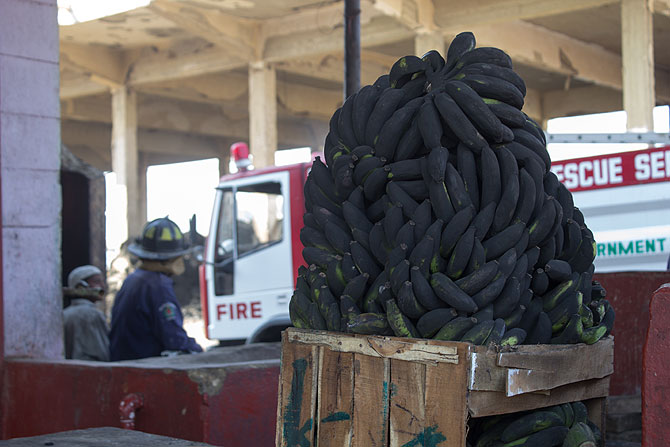 Fire men work outside a fruit shop at New Sabzimandi. In the foreground burnt bananas lie in a pile.