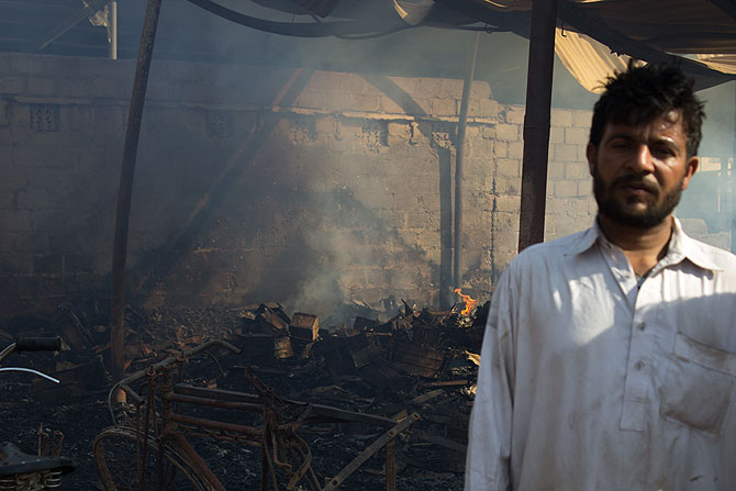 A shopkeeper looks on as a cycle workshop behind him is still burning a day after the blaze.