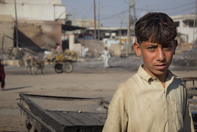 A boy from the area looks on. Behind him life moves on for the vegetable sellers in the area.