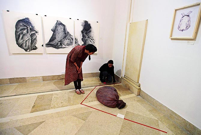 Visitors look at a latex russet-coloured sack designed to feel like human skin, at an exhibition.