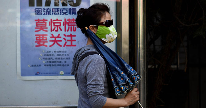 A woman wears a face mask as she walks past a poster showing how to avoid the H7N9 avian influenza virus, by a road in Beijing on April 24, 2013. — Photo AFP