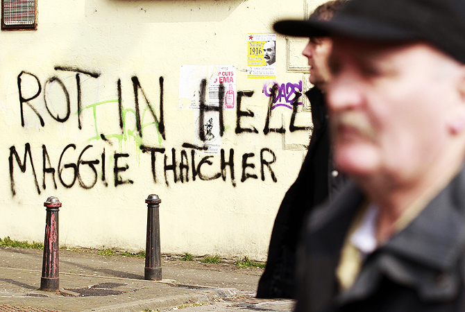 Men pass graffiti daubed on a wall referring to the death of former prime minister Margaret Thatcher, on the Falls Road in west Belfast.