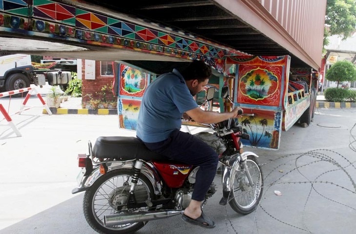 A motorcyclist ducks to go under a shipping container placed by security forces to stop protesters from entering the capital, Islamabad, as he drives on a street in Lahore on Wednesday — AP Photo