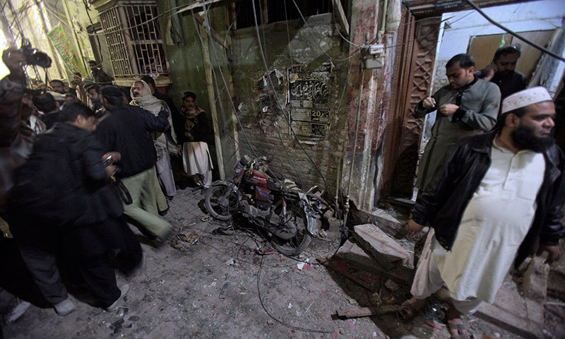 A police officer and local residents gather next to a damaged motorcycle at the site of a blast in Rawalpindi on Jan 9, 2015. – AP