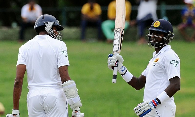 Sri Lankan cricket captain Angelo Mathews (R) is watched by his teammate Jehan Mubarak (L) as he raises his bat to the crowd after scoring a half-century (50 runs) during the third day of the third and final Test cricket match between Sri Lanka and Pakistan at the Pallekele International Cricket Stadium in Pallekele on July 5, 2015. — AFP