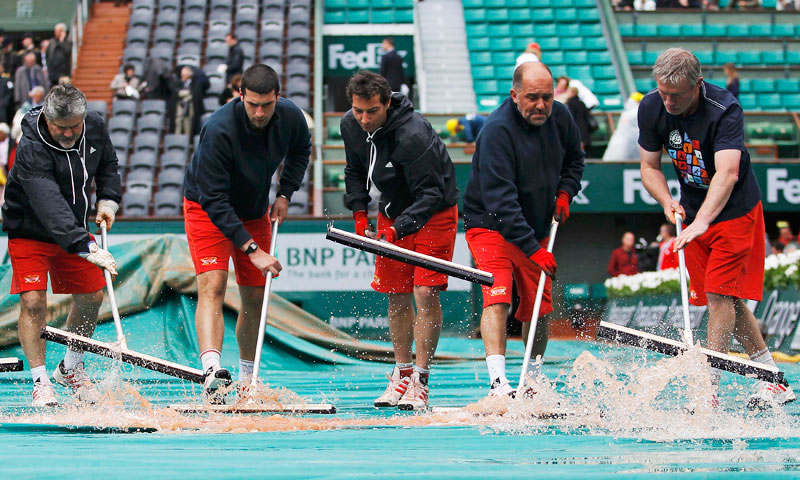 Workers sweep water from a tarp covering a court during a rain delay. —Reuters Photo