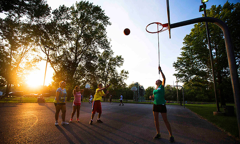 Counselor Stephanie Connolly (R) uses a white cane causing noise on the basketball rim to help direct Jordan Vieira (C) to shoot the basketball in the direction of the net at Camp Abilities in Brockport, New York.