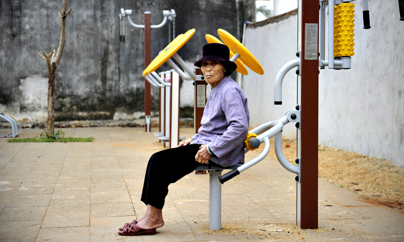 An elderly woman sitting on an exercise equipment in Chengmai city.