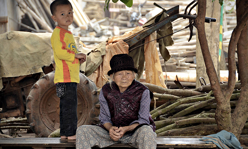 An elderly woman looking on as she having a rest with a boy by a road in Chengmai city.