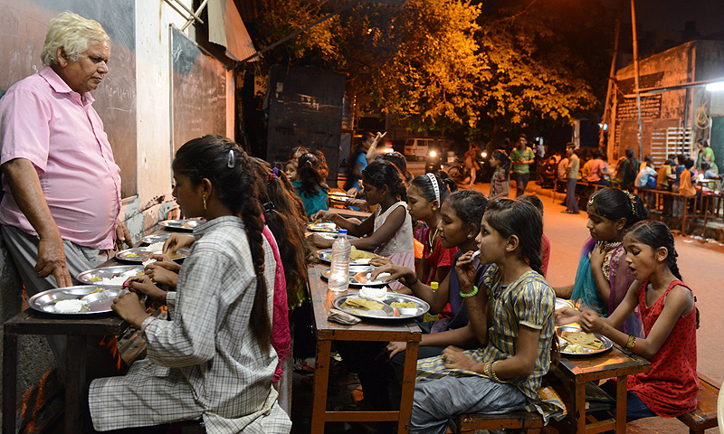 Indian teacher Kamalbhai Parmar,66, watches students eat a meal at the Footpath School in Ahmedabad. The Footpath School was started by Parmar, who runs a metal fabrication business and has been teaching his students on a footpath for the past twelve years. Parmar and his sons started the school for children of labourers, ragpickers and domestic servants so the children could receive extra education and a meal free of cost.—Photo by AFP