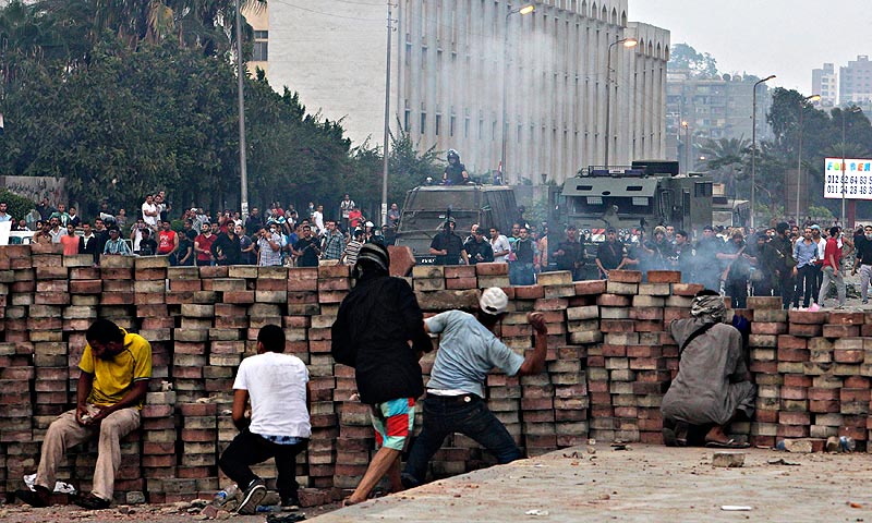 Morsi supporters throw stones from behind a makeshift barricade they built as they take cover from the police. — Reuters Photo