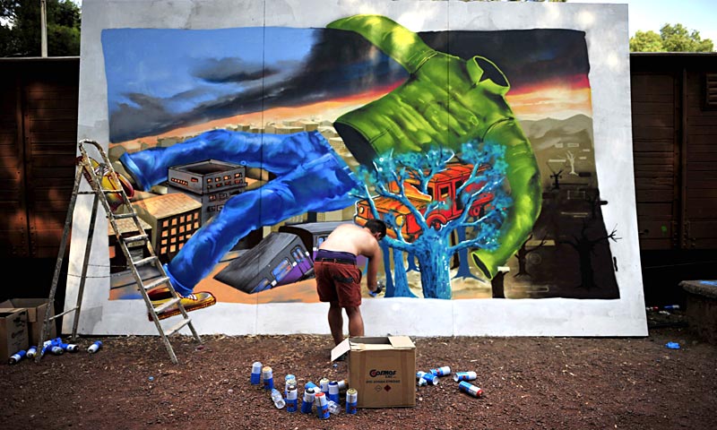 A street artist is pictured spraying paint on artwork during a street festival in the central square of Kalamata, southern Greece. — AFP Photo