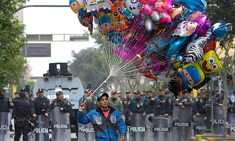 A balloon vendor walks in front of a group of riot police standing guard during an anti-government demonstration that was taking place as Peru's President Ollanta Humala delivered his State of the Nation address, in Lima. — AP Photo