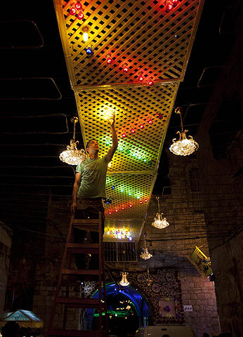 A Palestinian fixes lights in an illuminated street outside the Al-Aqsa mosque compound in the old city of Jerusalem. — AFP Photo