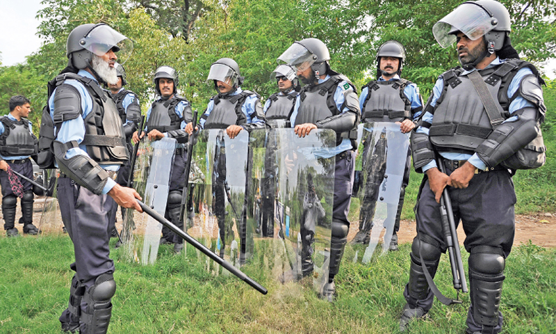 Capital police personnel in riot gear stand on a greenbelt in Islamabad on Saturday — Photo by Tanveer Shahzad