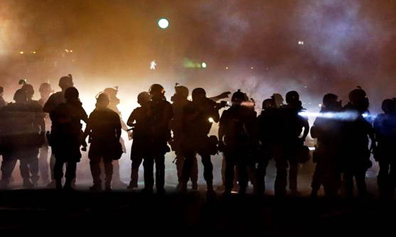 Police walk through a cloud of smoke as they clash with protesters in Ferguson.  —Photo by AP