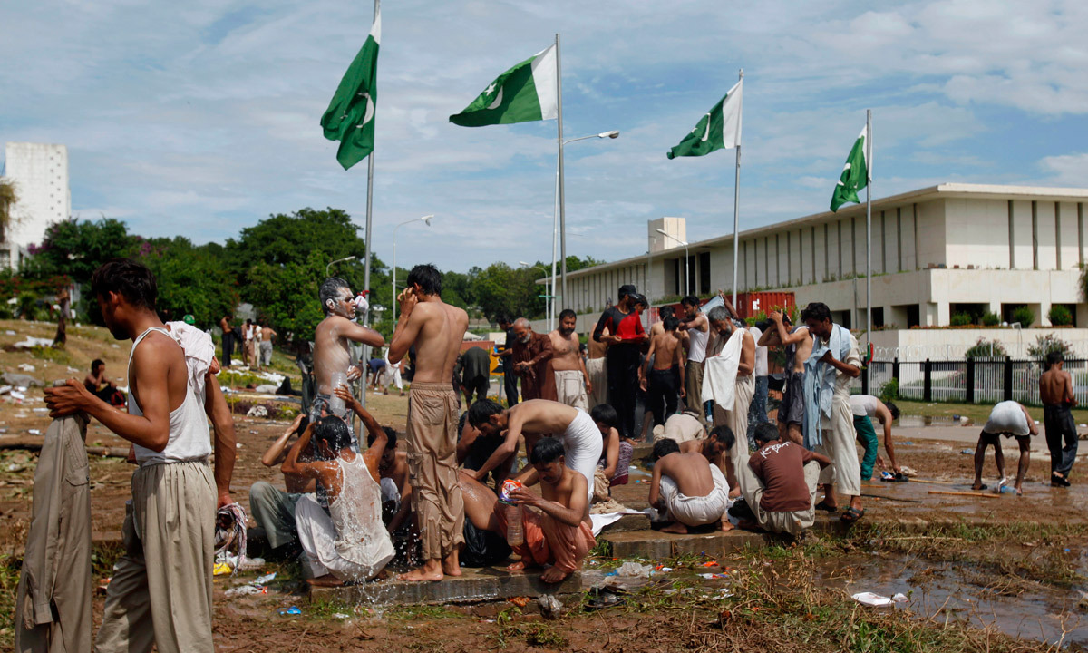 Protesters bathe at a leaking water supply line close to the parliament building where they are camped in Islamabad. - Photo by AP