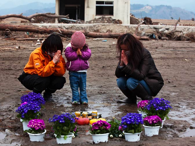 Two-year-old Ayaka (C) and family members pray for her missing grandmother and great-grandmother at a vacant lot where they lived. – Photo by AFP