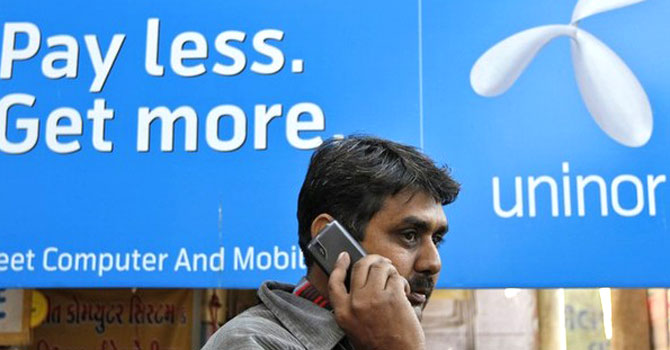 A man speaks on a mobile phone as he walks past a Uninor board in Ahmedabad. was among eight mobile operators whose licences granted in 2008 were cancelled by the Supreme Court in January on grounds the sale was under-priced and corrupt in what has become one of the biggest scandals in India’s history. – File photo by Reuters