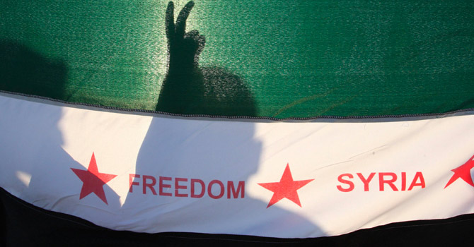 Syrian protesters are silhouetted behind a Syrian opposition flag.—Reuters Photo