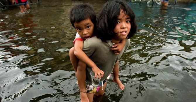 A girl holds a boy on her back to help him cross the floodwaters in a street in Valenzuela. — AFP Photo