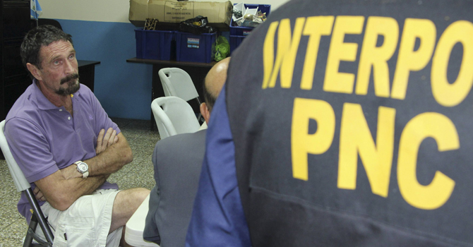 U.S. anti-virus software guru John McAfee sits next to an INTERPOL agent after his detention in Guatemala City