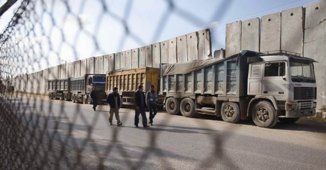 Palestinians walk past trucks loaded with gravel at the Kerem Shalom crossing between Israel and the southern Gaza Strip Dec 30, 2012. - Reuters