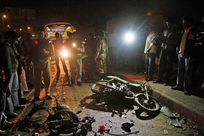 A Pakistani police officer, left, talks on the radio while cameramen flim the site of a blast in Karachi, Pakistan, Tuesday, Jan. 1, 2013. - Photo by AP