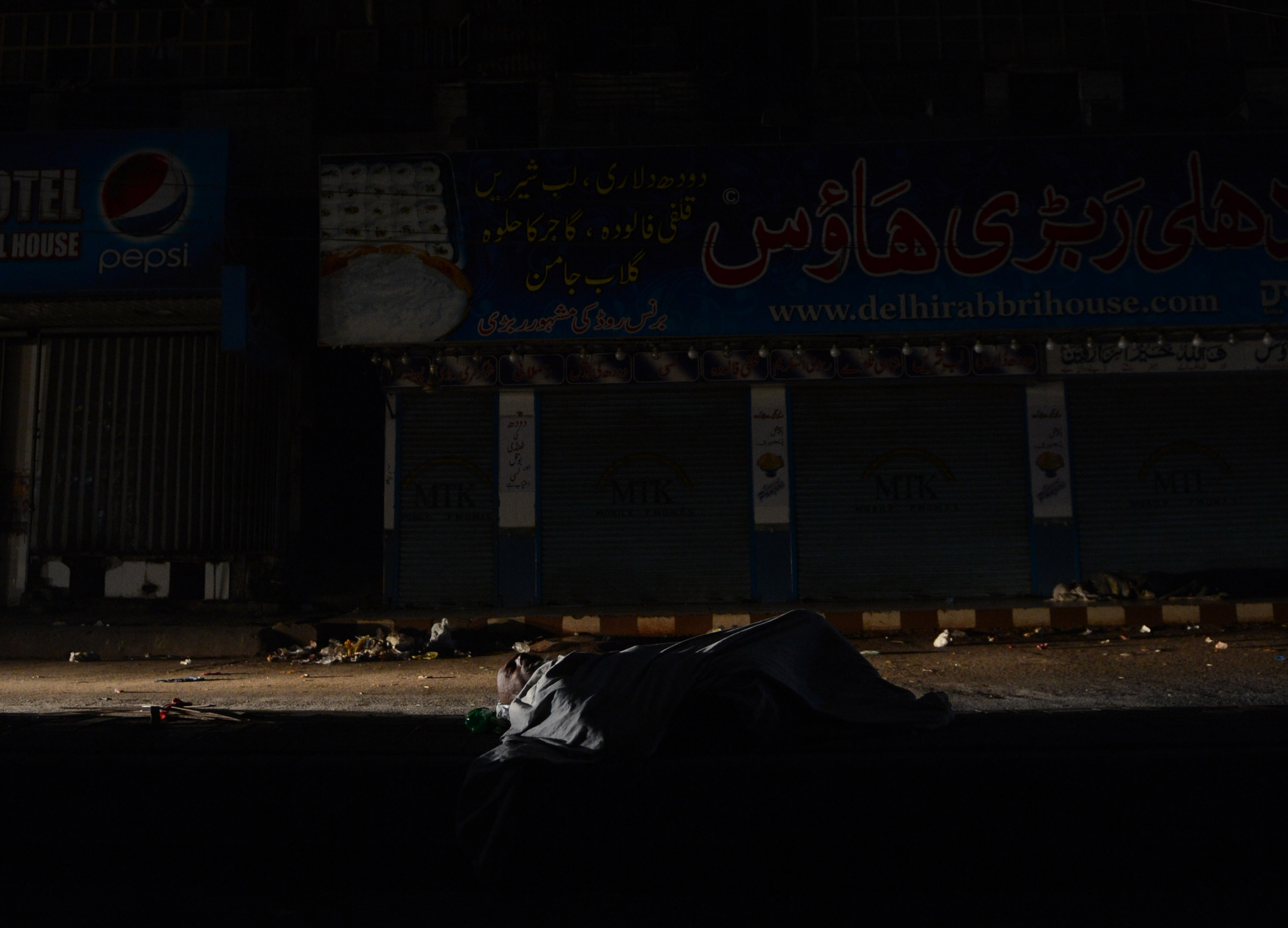 This picture taken on February 24, 2013 shows a homeless Pakistani man sleeping on a roadside during a nationwide power blackout in Karachi. Pakistan was hit by a nationwide blackout for more than two hours after the breakdown of a major plant caused power stations to stop working across the country, officials said on February 25.  AFP PHOTO/Asif HASSAN